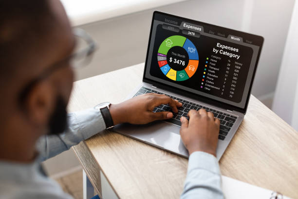 High-Angle Back View Of Black Businessman Using Laptop, Typing On Keyboard, Sitting At Workplace In Modern Office, Working On Family Budget, Checking Expenses Online, Creative Image